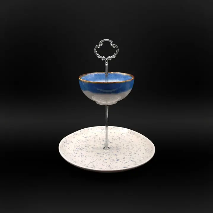 Zweistufige Etagere mit silberfarbenem Metallständer, oben eine blau glasierte Schale mit braunem Rand, unten ein weißer Teller mit blauen Sprenkeln, vor schwarzem Hintergrund.