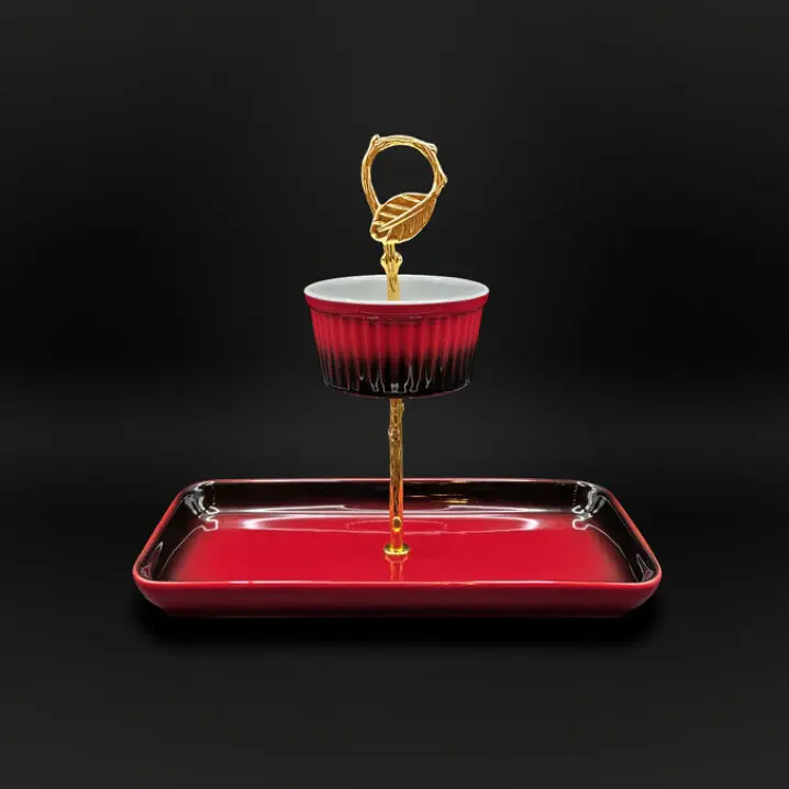 Servier-Set mit rechteckigem, dunkelrotem Tablett und goldfarbenem Ständer; oben eine rot-weiße Schale, der Griff ist als goldener Ring mit Blatt gestaltet, vor schwarzem Hintergrund.