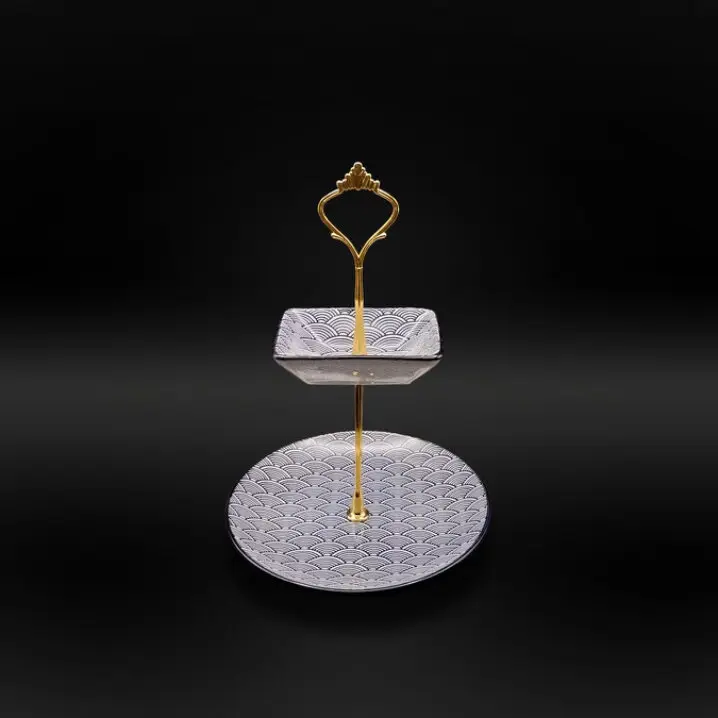 Zweistufige Etagere mit goldfarbenem Metallgriff; oben quadratischer Teller, unten runder Teller mit schwarz-weißem Wellenmuster, vor schwarzem Hintergrund.