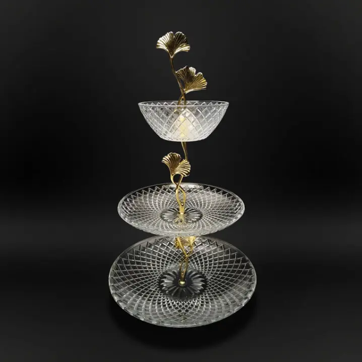 Dreistöckige Etagere mit goldfarbenen Ginkgo-Blattgriffen und gläsernen, facettierten Tellern vor schwarzem Hintergrund