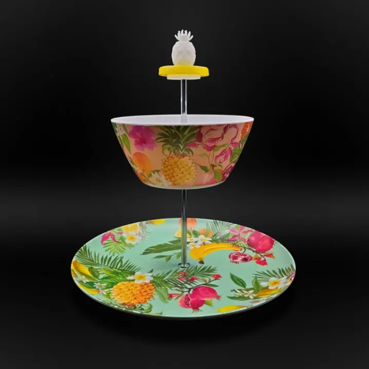 Zweistufige Etagere mit bunter Obst- und Blumenmusterung; oben eine Schale, unten ein Teller, Metallstange mit Ananas-Griff, vor schwarzem Hintergrund.