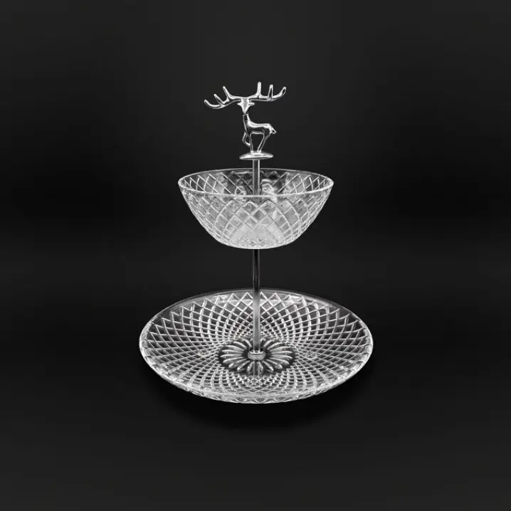 Zweistufige Glas-Etagere mit geschliffenem Rautenmuster, Metallstange und Hirschfigur als Griff, vor schwarzem Hintergrund.