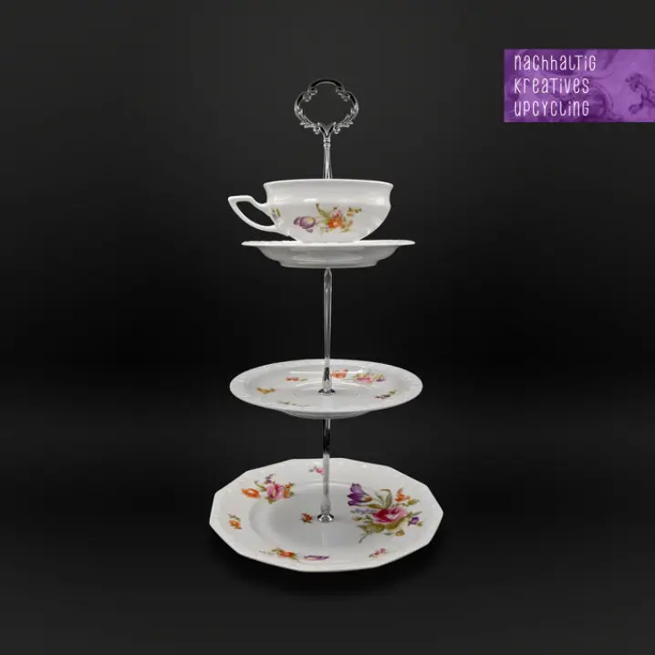 Dreistufige Etagere aus Upcycling-Porzellan: oben eine Tasse als Schale, darunter zwei Teller mit Blumenmuster, verbunden durch eine silberfarbene Metallstange; oben rechts Schriftzug „nachhaltig kreatives upcycling“.<br />