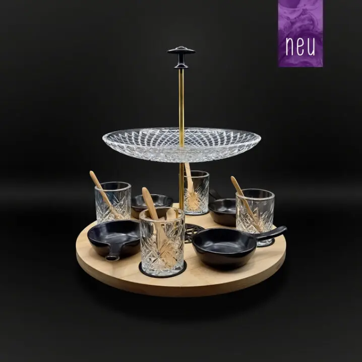 Servier-Set mit großer Glas-Etagere auf goldfarbener Stange, rundem Holztablett, vier schwarzen Schälchen und vier Gläsern mit Löffeln vor dunklem Hintergrund.